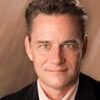 Jeff Hull headshot photo, smiling man wearing black blazer and light button up shirt in front of neutral background