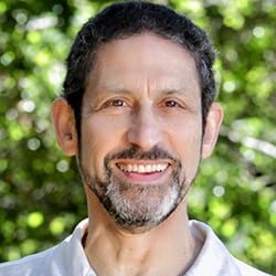 Lion Goodman PCC headshot photo, smiling man wearing a light colored collared shirt in front of greenery
