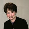 Wilma Fellman headshot photo, smiling woman with short dark hair wearing dark top in front of neutral background