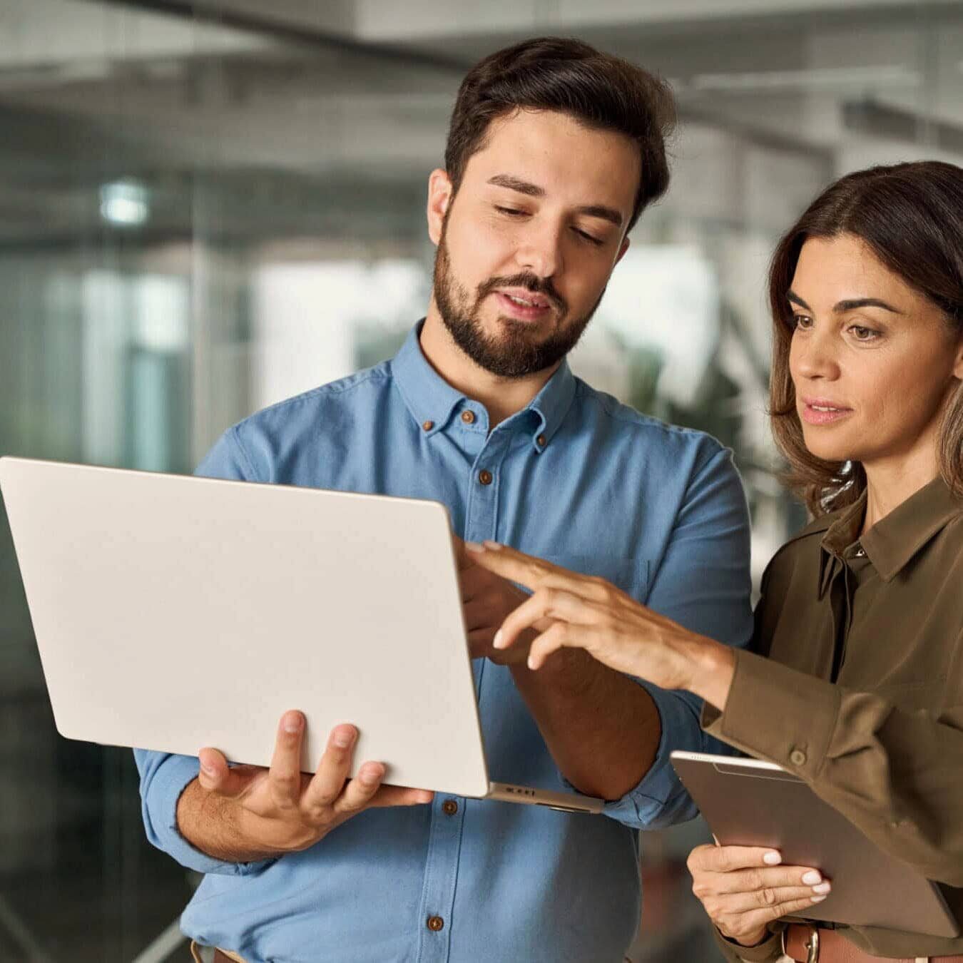 A man and woman compare notes on their computer and tablet in an office.