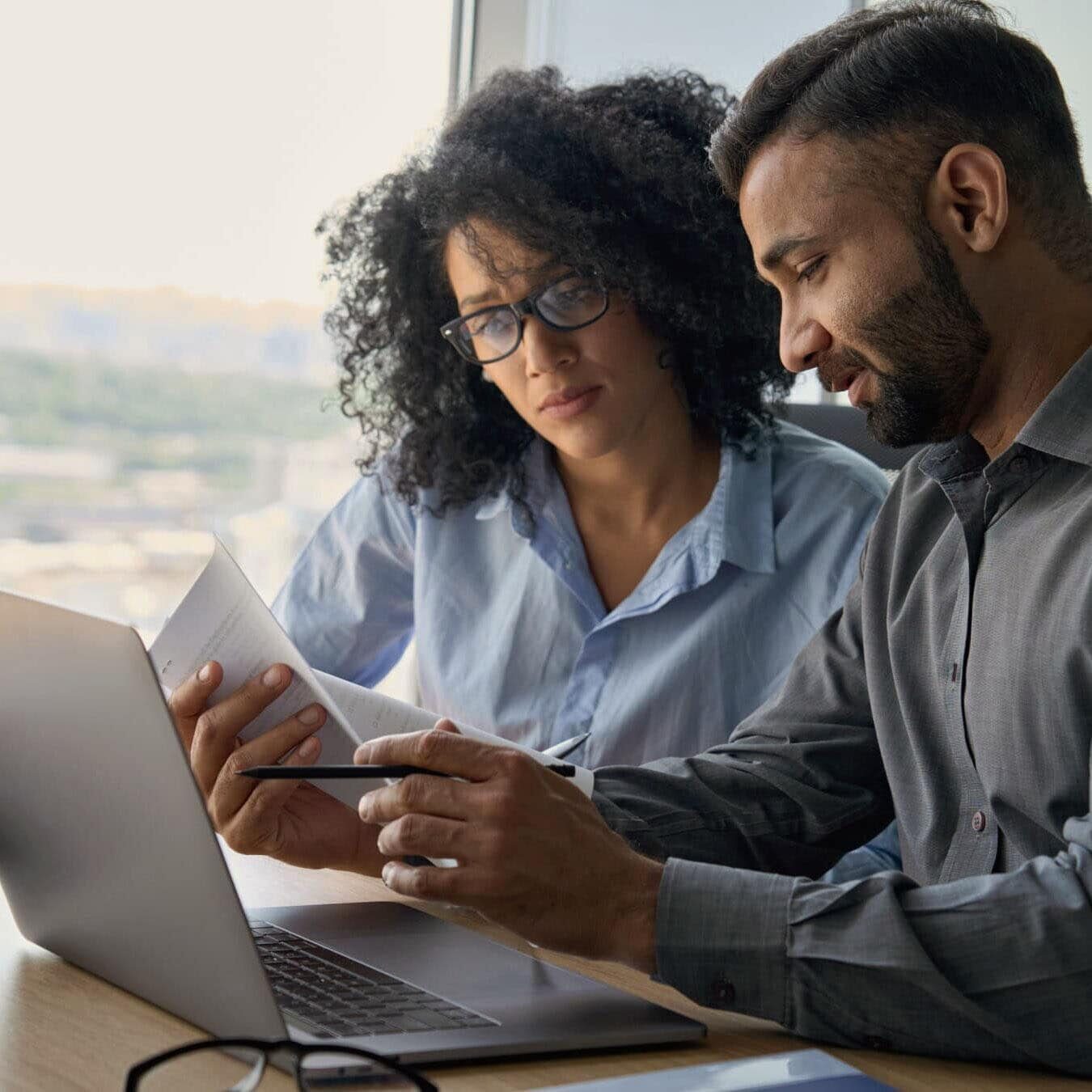 A man and woman review information on a computer screen in a casual office.