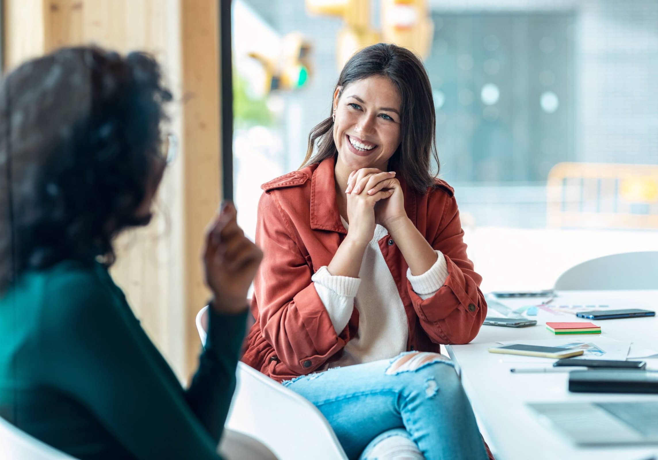 Two women having a focused discussion at a table with a laptop open in front of them.