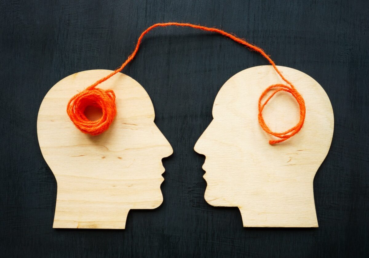Two wooden head silhouettes connected by a piece of orange thread or string.