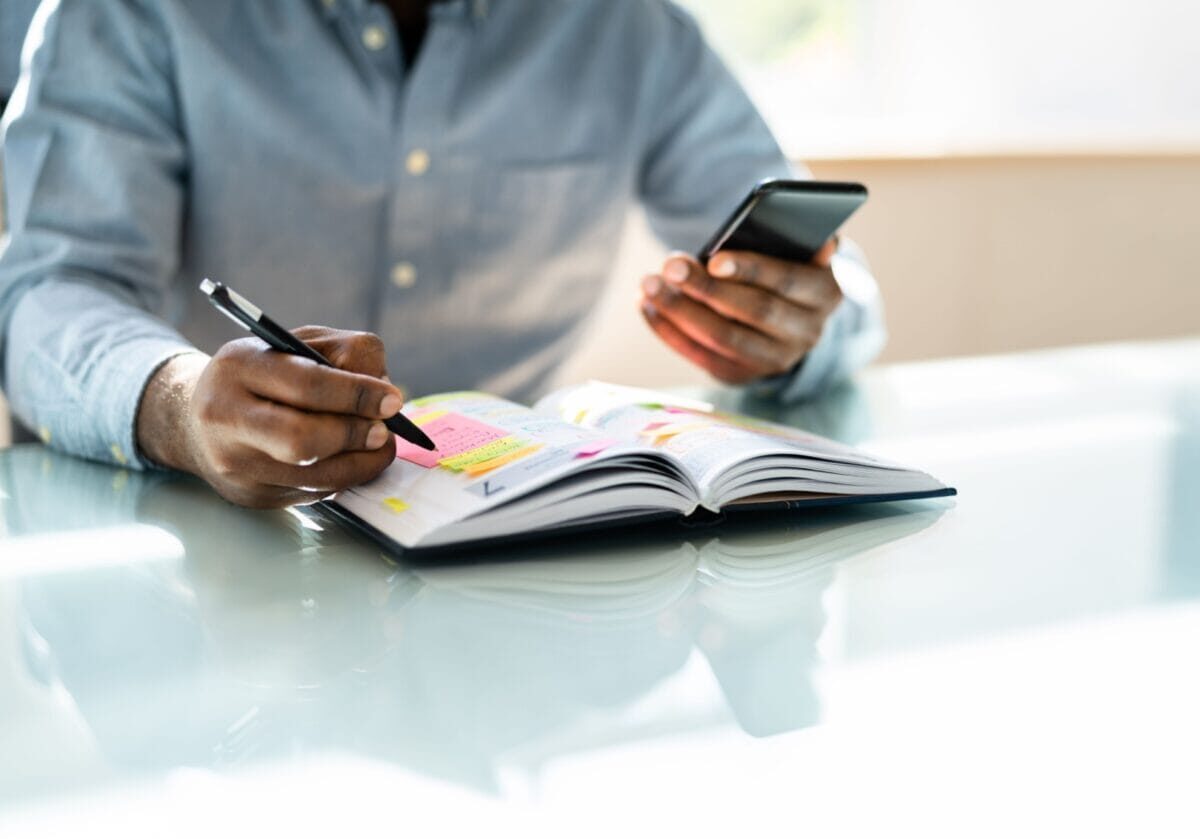 A professional coach reviewing a color-coded planner while consulting a smartphone, planning a content strategy.