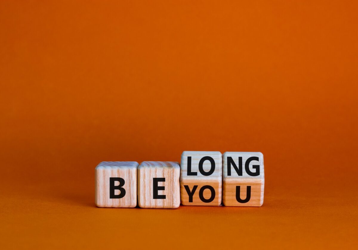 Wooden letter blocks spelling 'Be Long' and 'Be You' on an orange background, representing belonging in coaching.