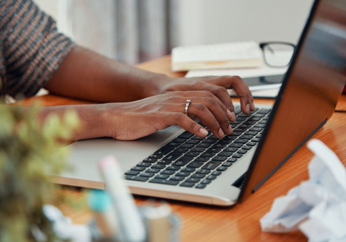 Close-up of hands typing on a laptop at a cluttered work desk