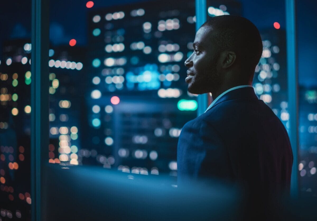 Smiling Black business leader looking out office window at city skyline, symbolizing leadership and vision in a changing energy landscape.