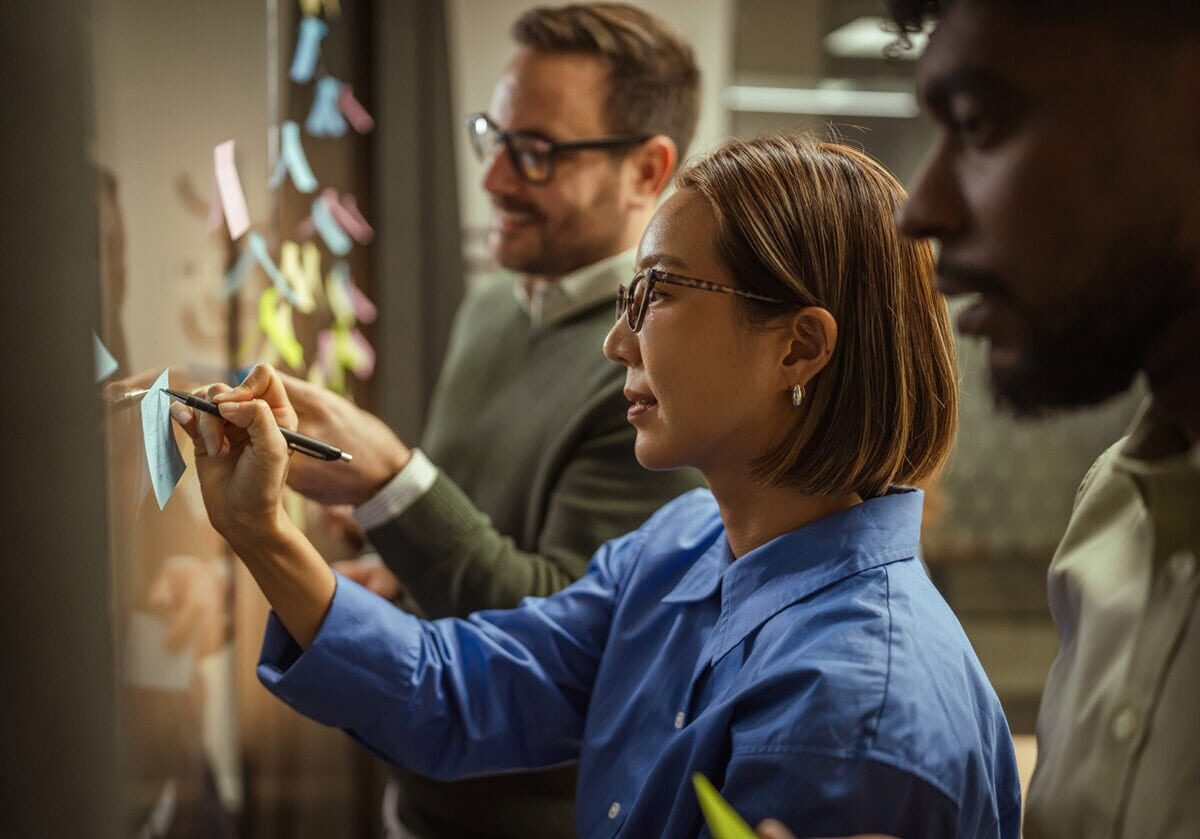 Diverse professionals placing notes on a glass wall during a collaborative planning session.