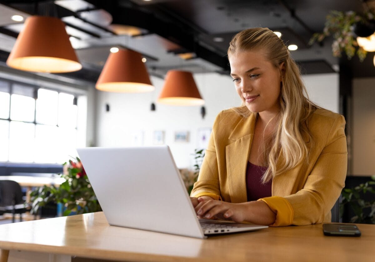 A professional coach working on a laptop in a modern workspace while creating LinkedIn content.