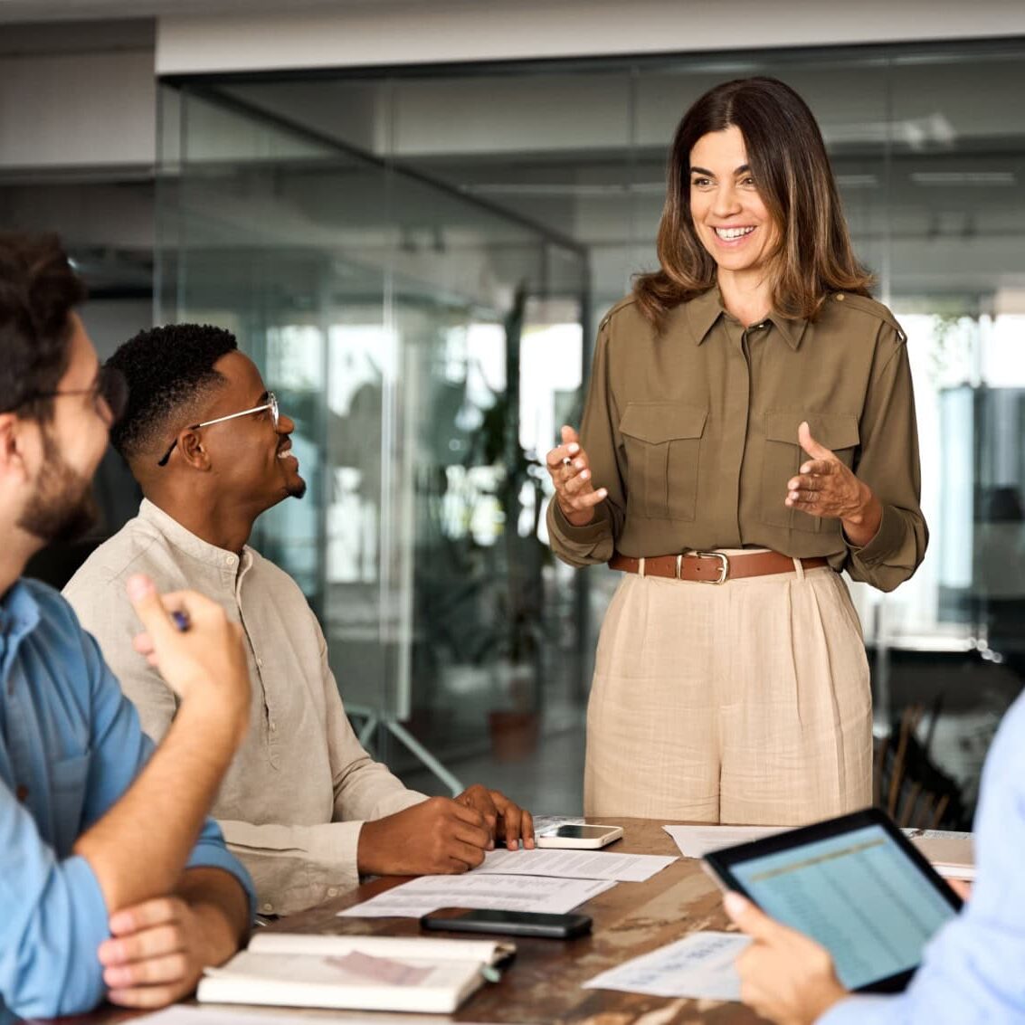 Smiling woman leading a meeting with three seated colleagues in a modern office.