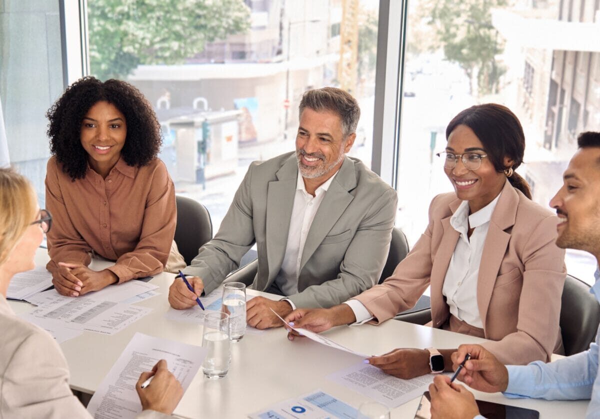 Diverse business leaders reviewing reports and discussing organizational performance and leadership strategy.