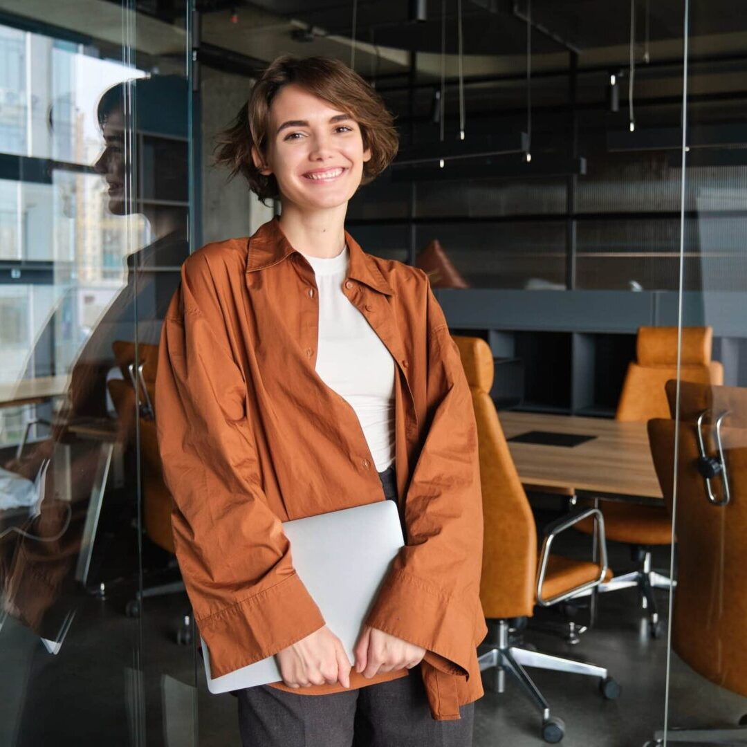 Woman holding laptop in a office looking at the camera, as she works to earn her MCS.