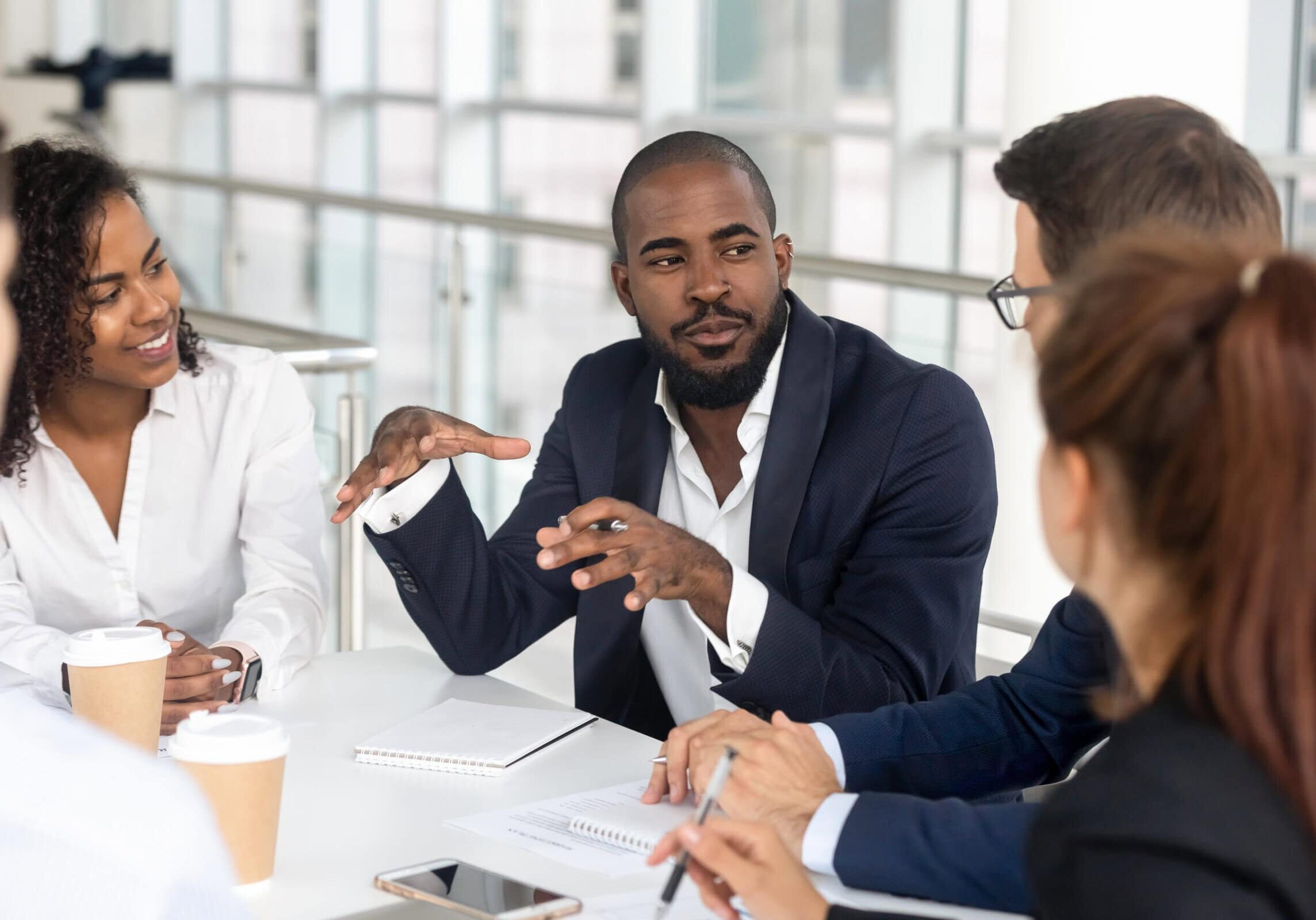 coach talking to a group of people around a table all looking at him and listening